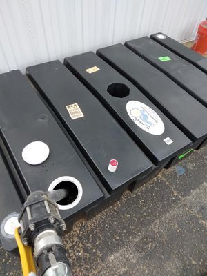 A nozzle fills one of several long, rectangular black plastic water tanks arranged side by side outdoors