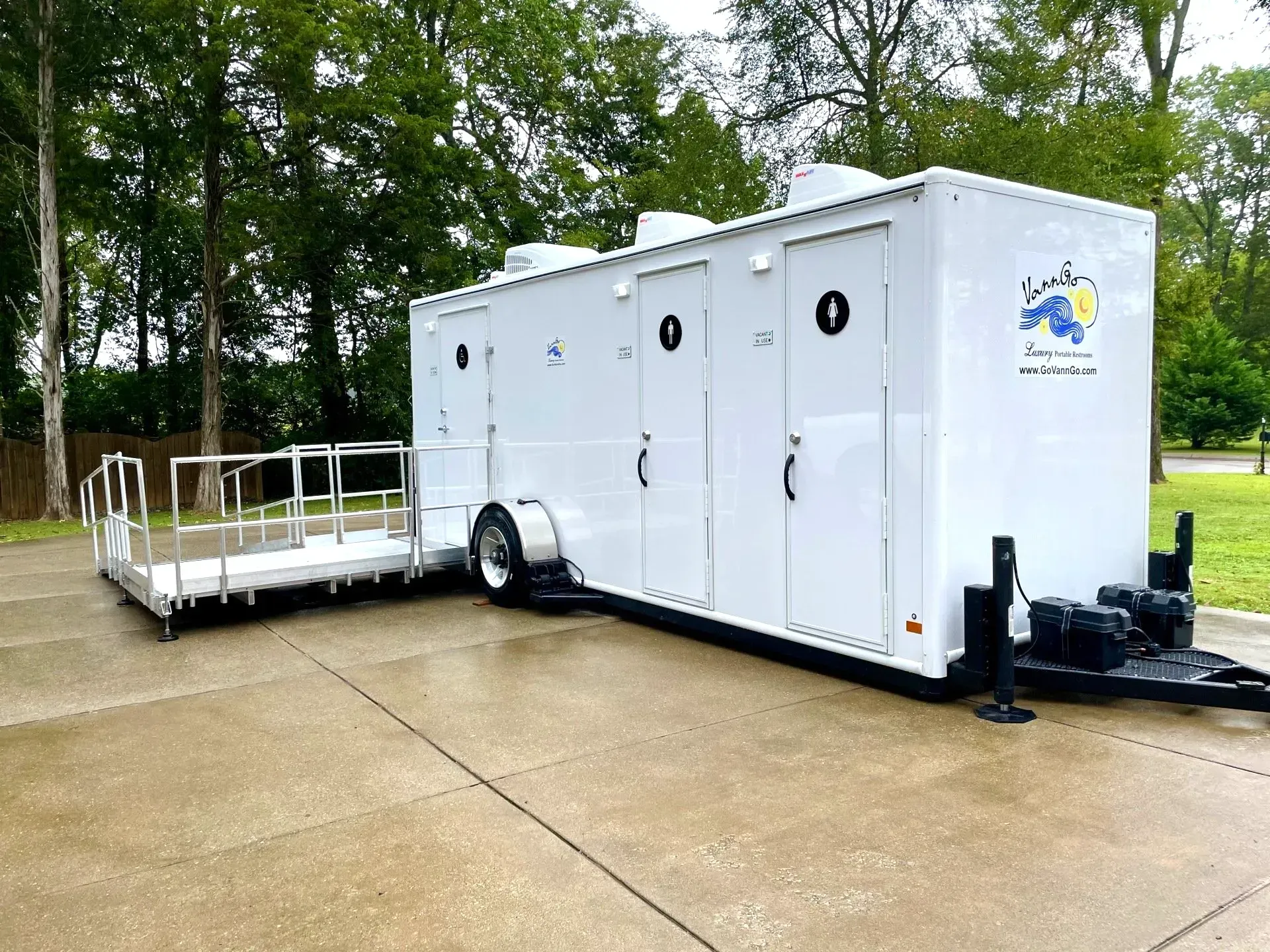 White portable restroom trailer with ramp, parked outdoors.