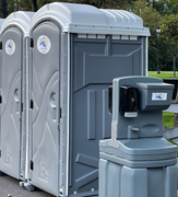 Three gray portable toilets and a handwashing station set outdoors.