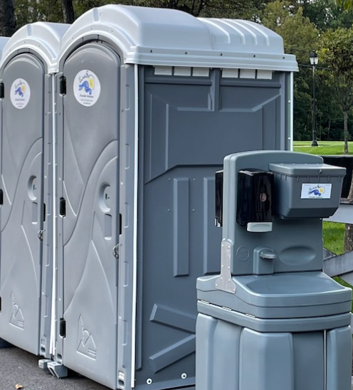 Three gray portable toilets and a handwashing station set outdoors.