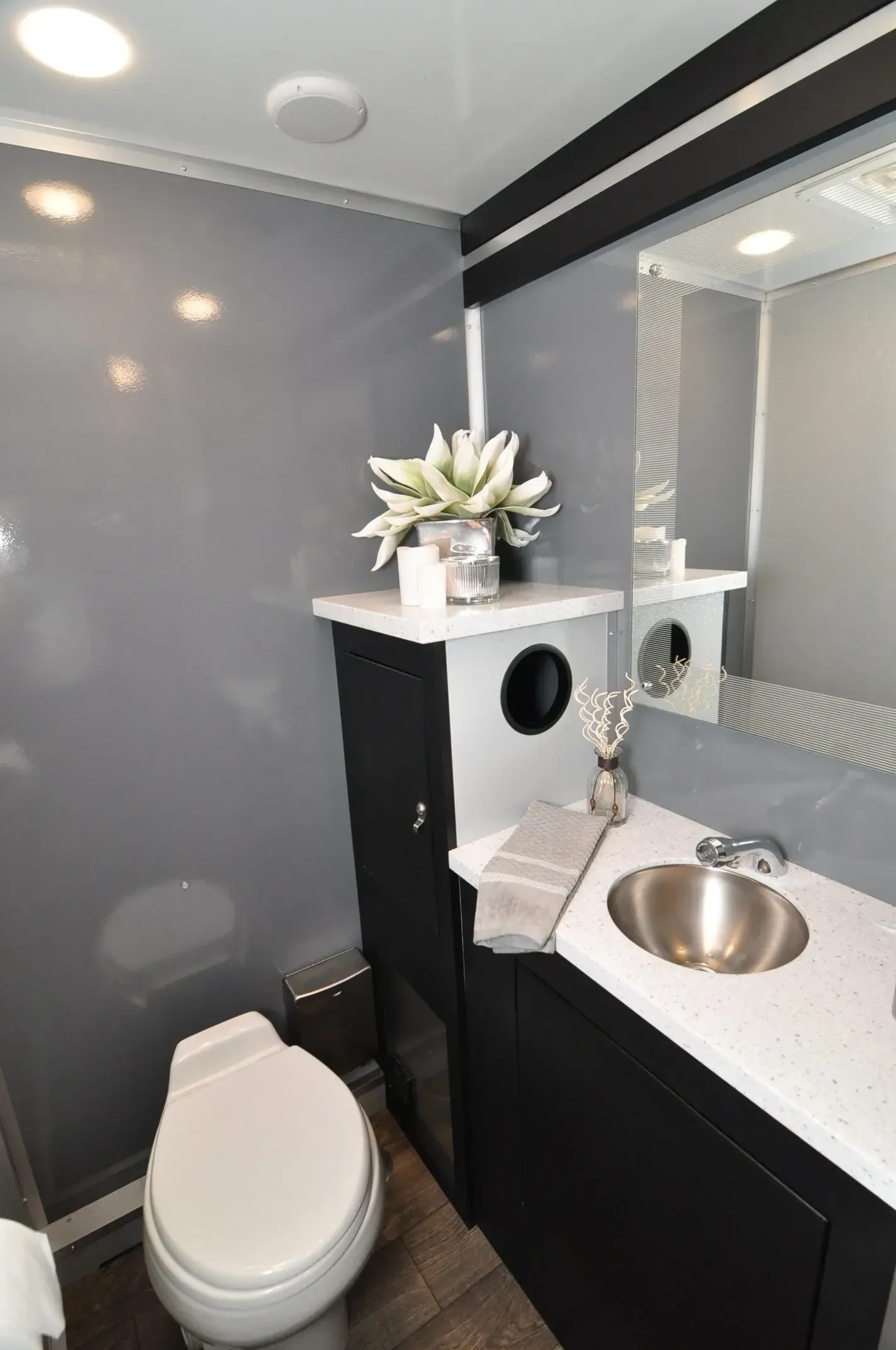 Interior of a luxury portable restroom with gray walls, black cabinets, and a white toilet.