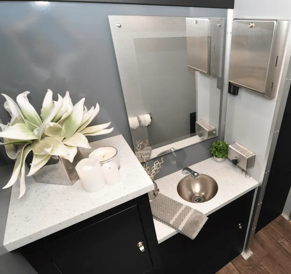 Modern restroom interior with gray walls, white countertop, stainless steel sink, mirror, and decorations.