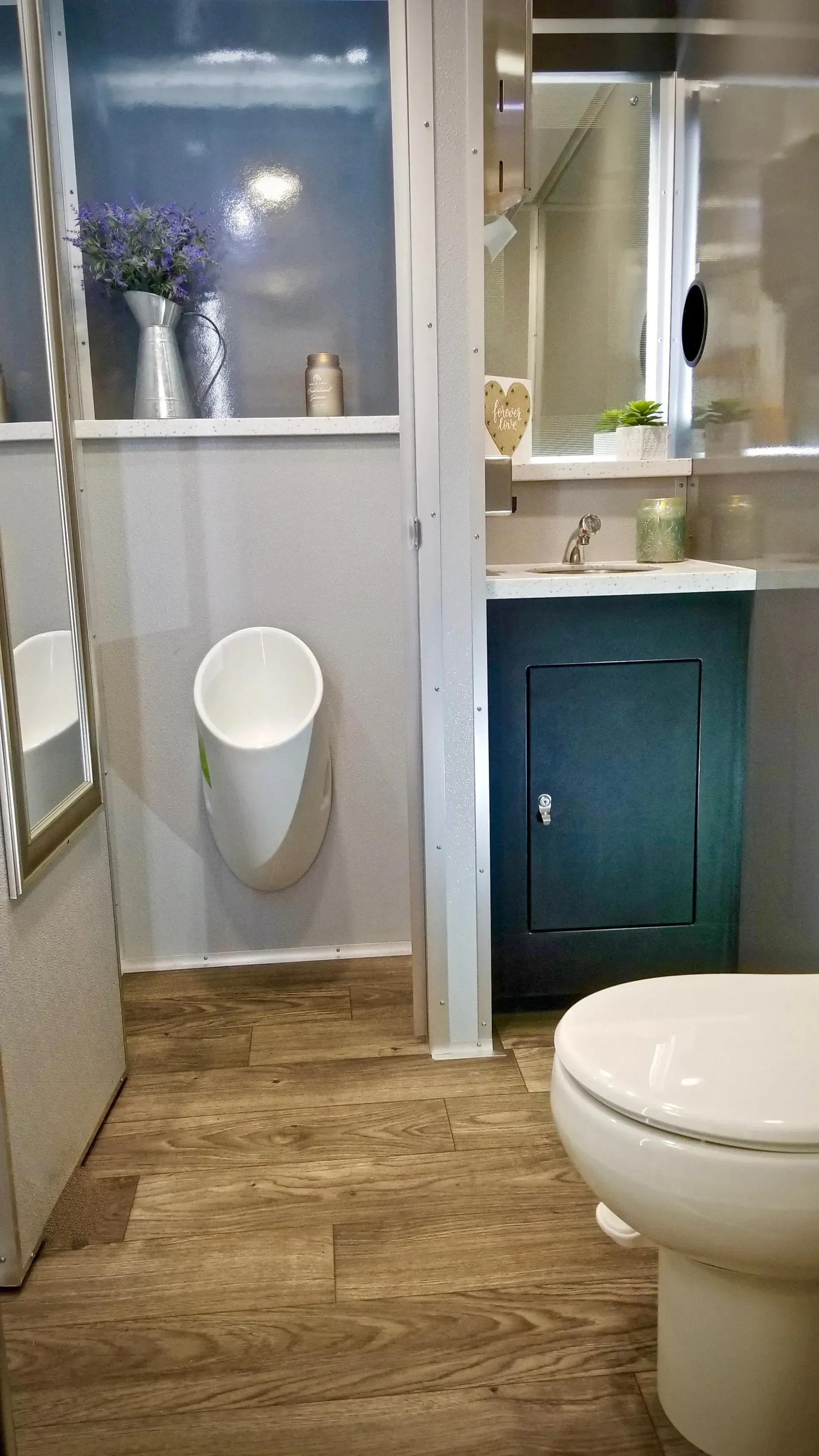 A small, remodeled bathroom with a urinal, vanity, and toilet. Light wood flooring and white walls.