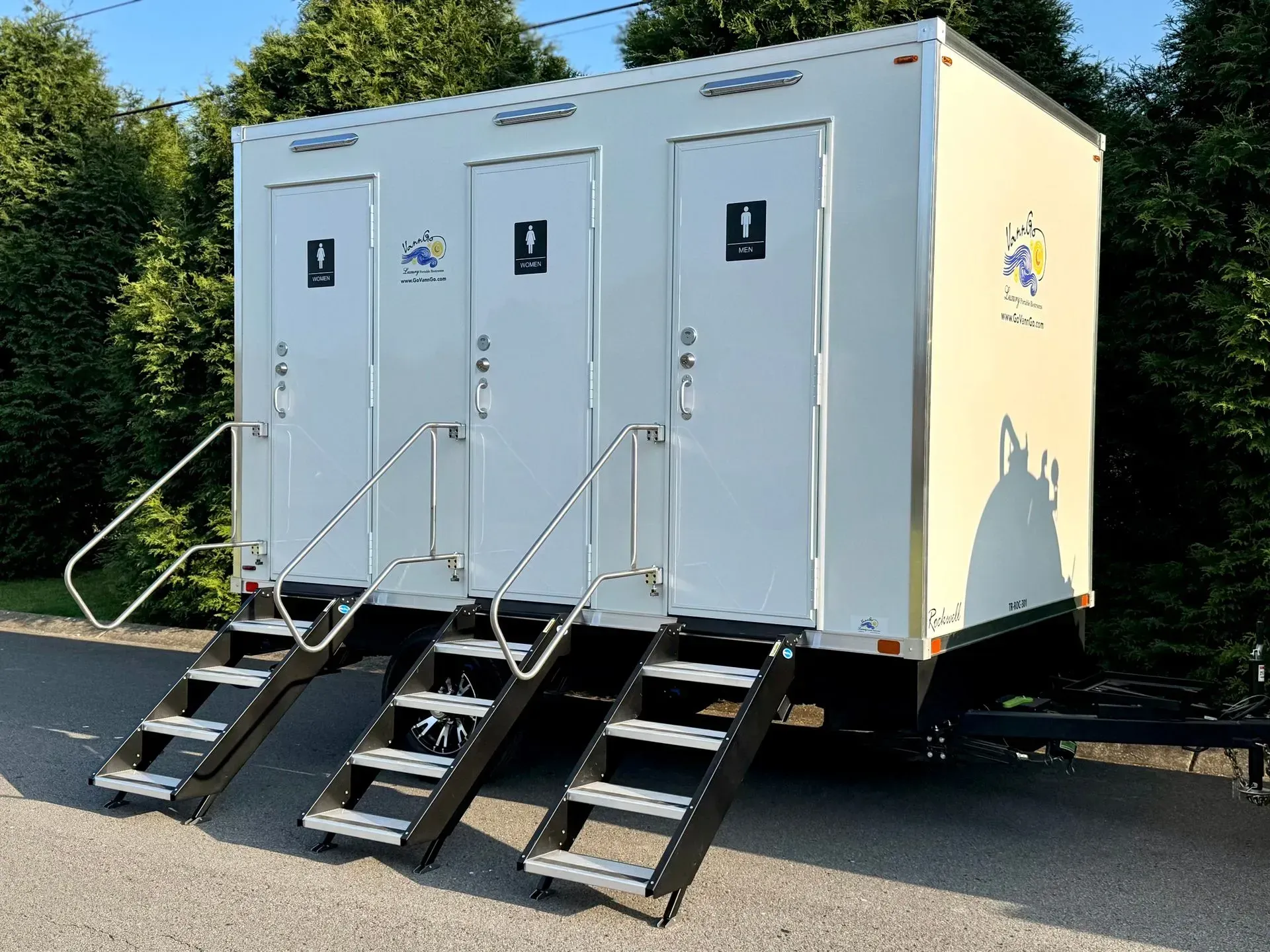 A portable restroom trailer with three individual stalls and steps.