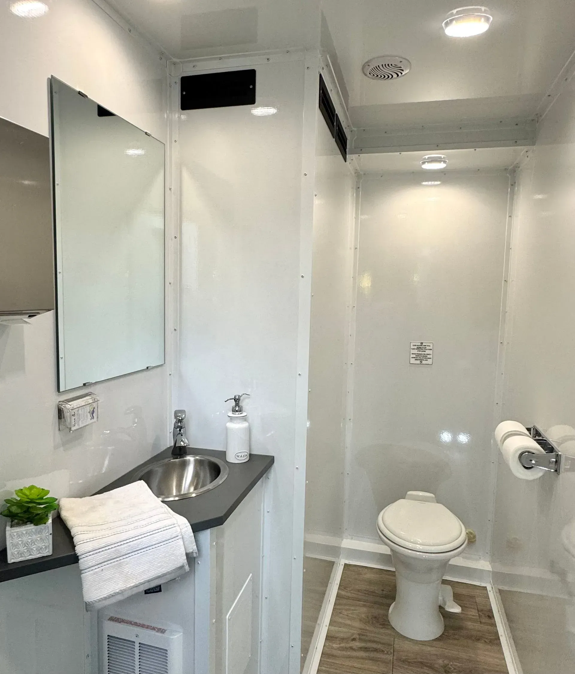 Interior of a modern, clean bathroom with a toilet, sink, mirror, and towels. White walls and neutral colors.