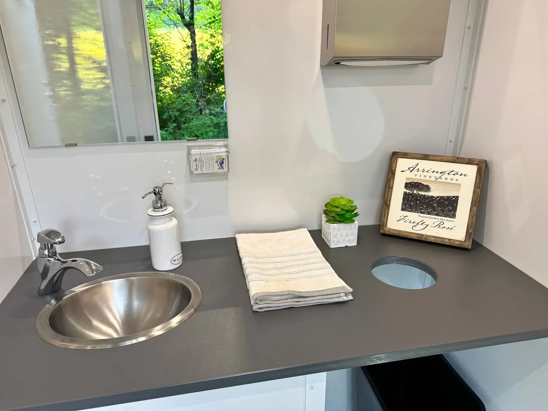 Bathroom sink and counter; window view, decorative items, and tissue dispenser.