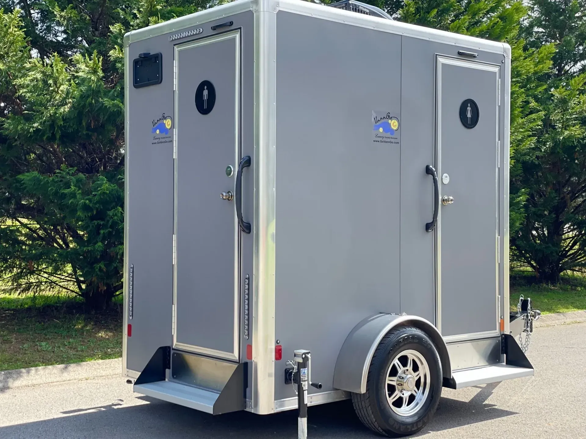 Gray portable restroom trailer with two separate stalls, set outdoors.