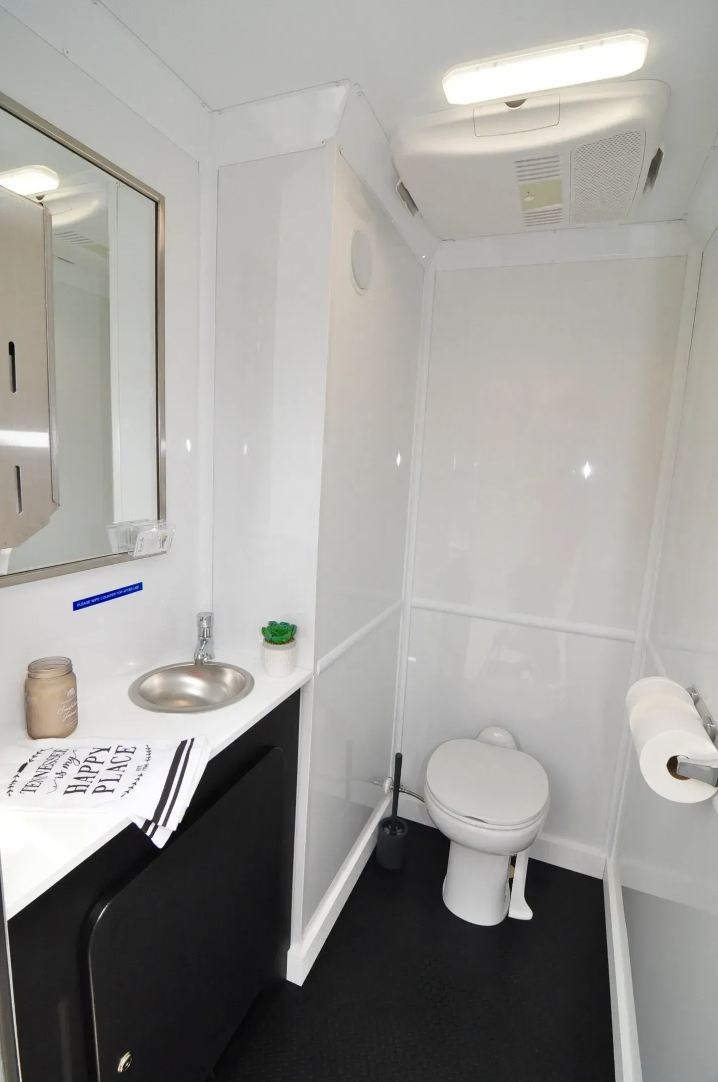 Interior of a clean, white portable toilet with a sink, mirror, and toilet paper roll. Black floor.