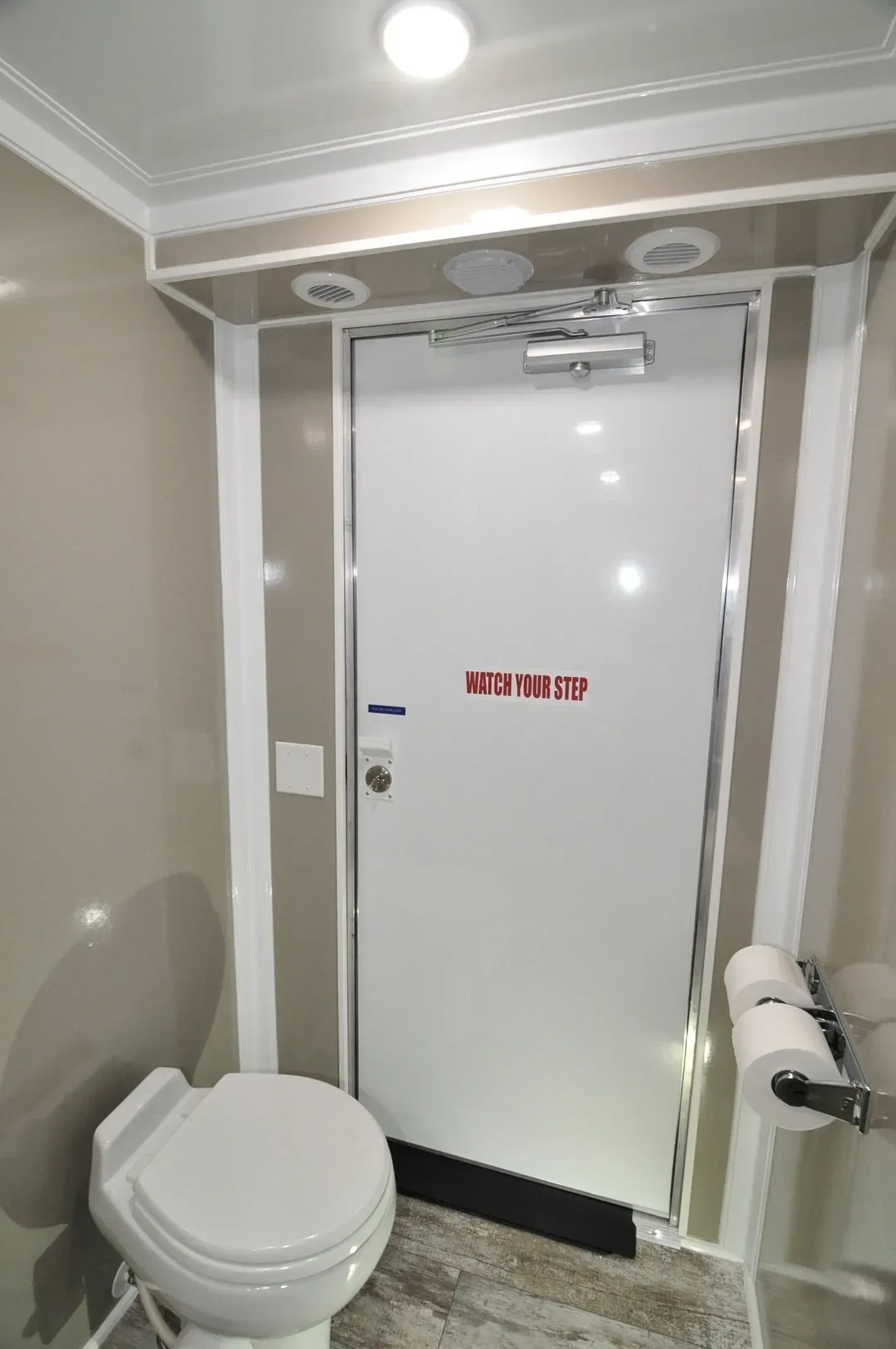Interior of a luxury restroom featuring a toilet, door with red text, and a roll of toilet paper.