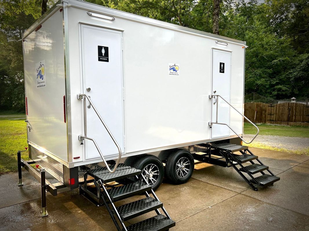 A white, two-stall portable restroom trailer with black steps and silver handrails.