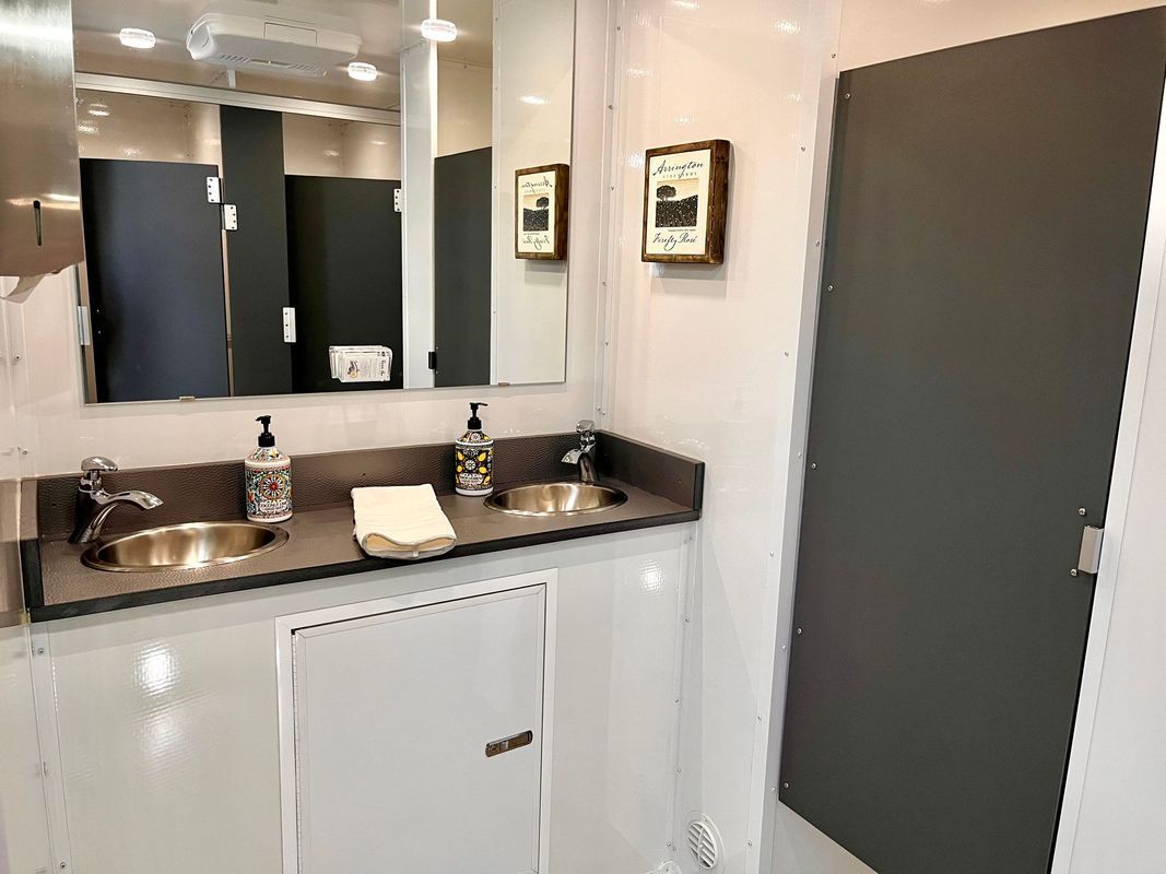 A clean, well-lit restroom with two sinks, mirrors, and individual stalls.