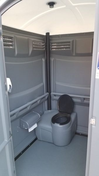 Interior of a gray portable toilet; includes toilet, toilet paper, and ventilation.