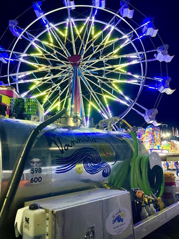 Ferris wheel lit with blue and yellow lights at night, next to a silver tank with a blue wave design.