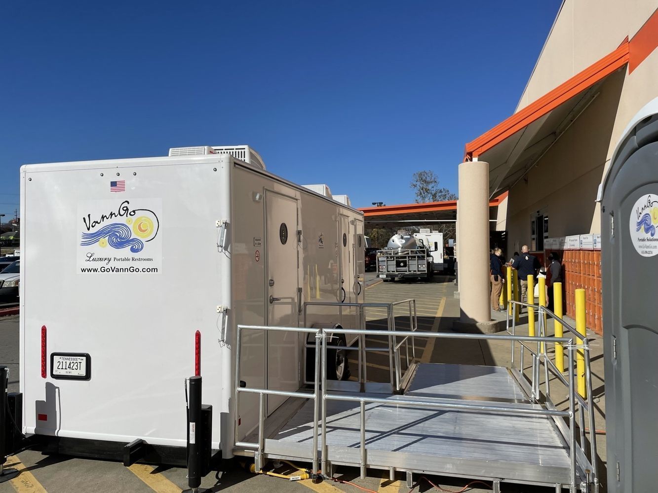 A white trailer with a wheelchair ramp parked beside a building.