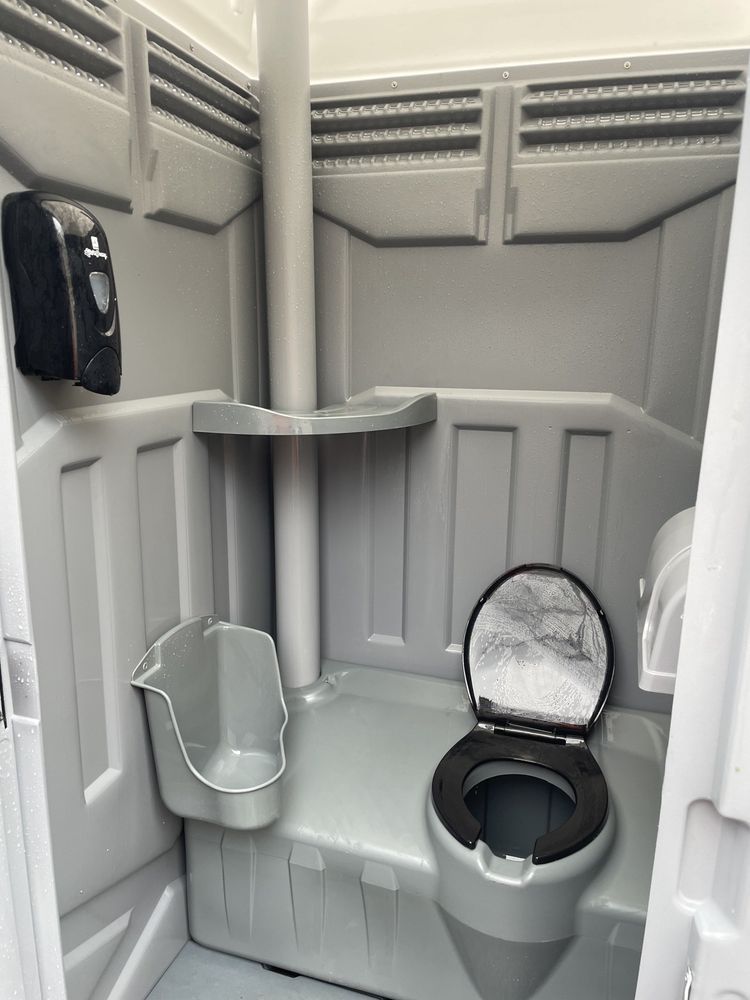 Interior of a portable toilet with gray walls, a urinal, a toilet, and a soap dispenser.