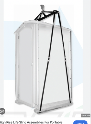 Portable toilet suspended by a black sling for high-rise transport. White enclosure, gray floor, black straps, sky.