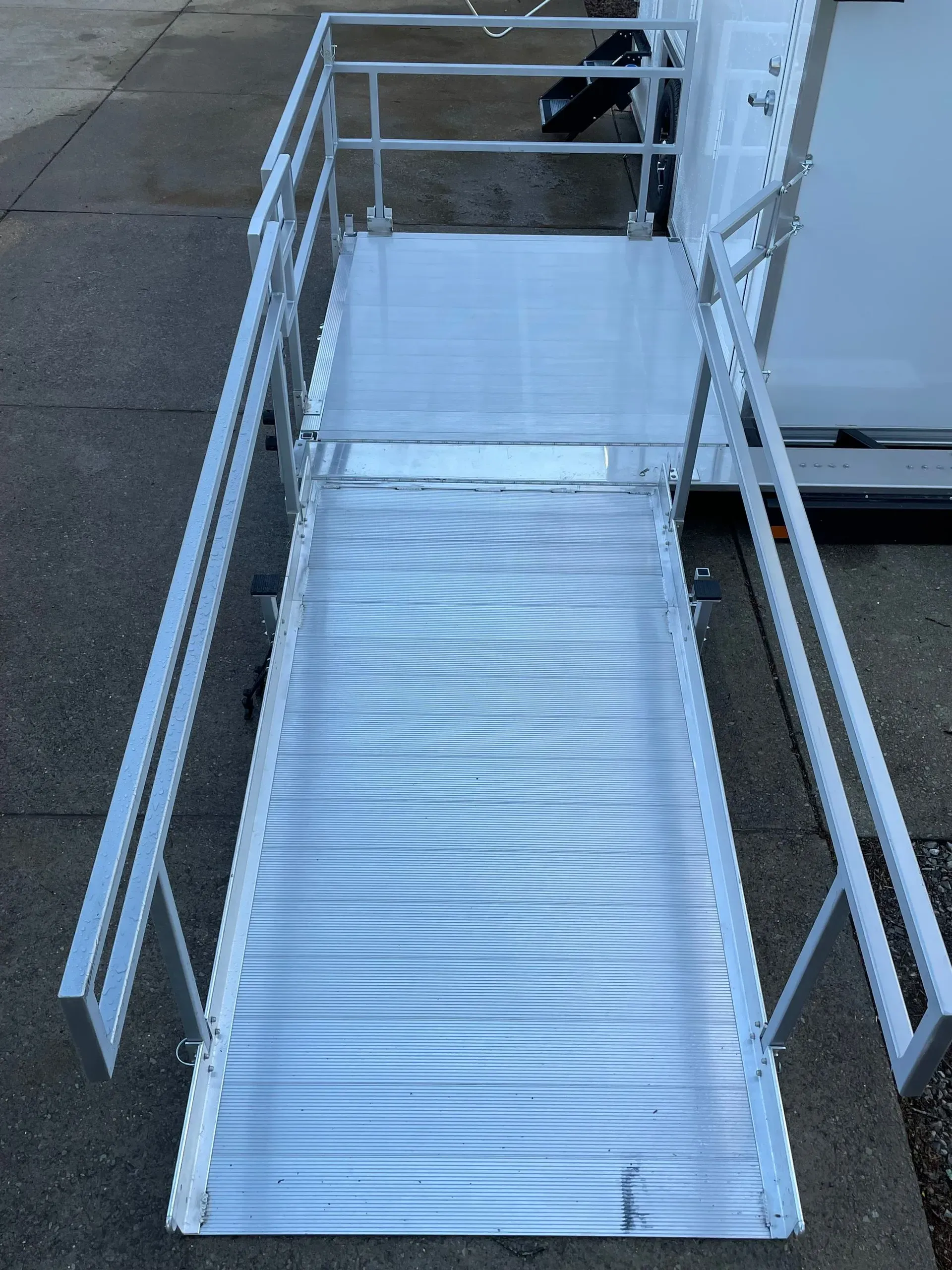 Silver aluminum ramp with railings and a platform, likely for accessibility, next to a white structure.