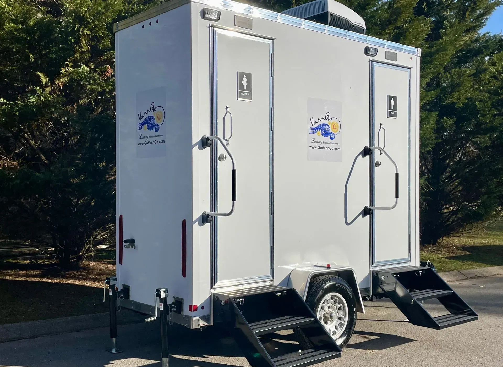 Portable restroom trailer with two separate stalls, white exterior, steps, and logo.