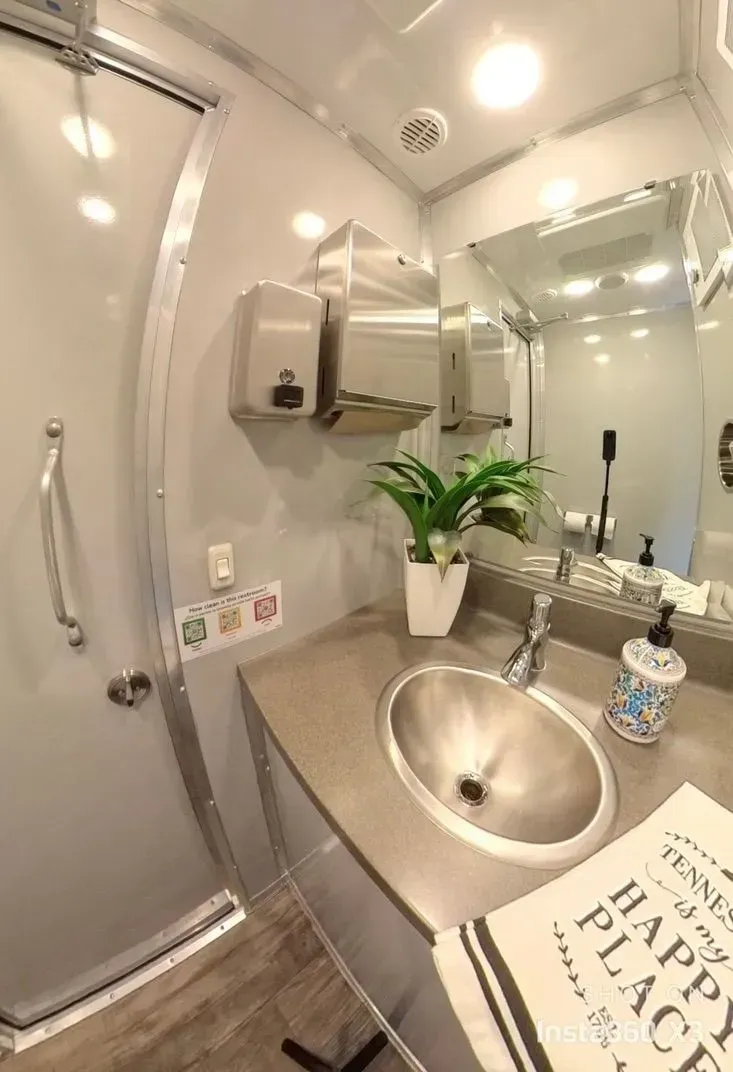 Inside of a luxury portable restroom. Sink, mirror, soap, paper towels, and a small plant are visible.