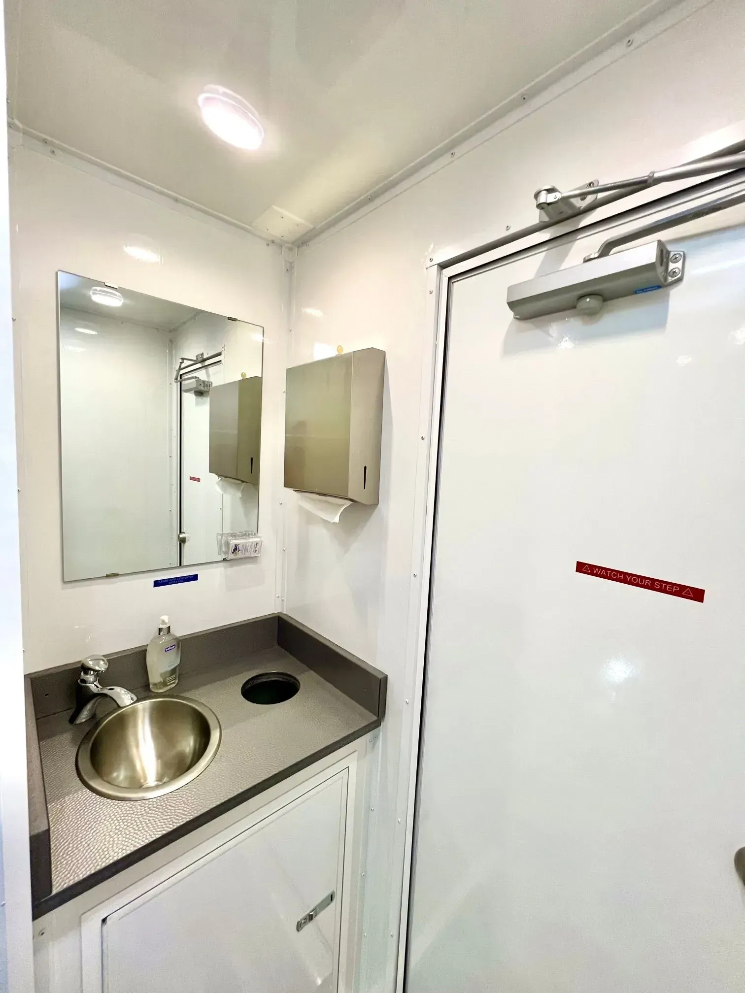 Interior of a white, accessible restroom with a sink, mirror, and paper towel dispenser.