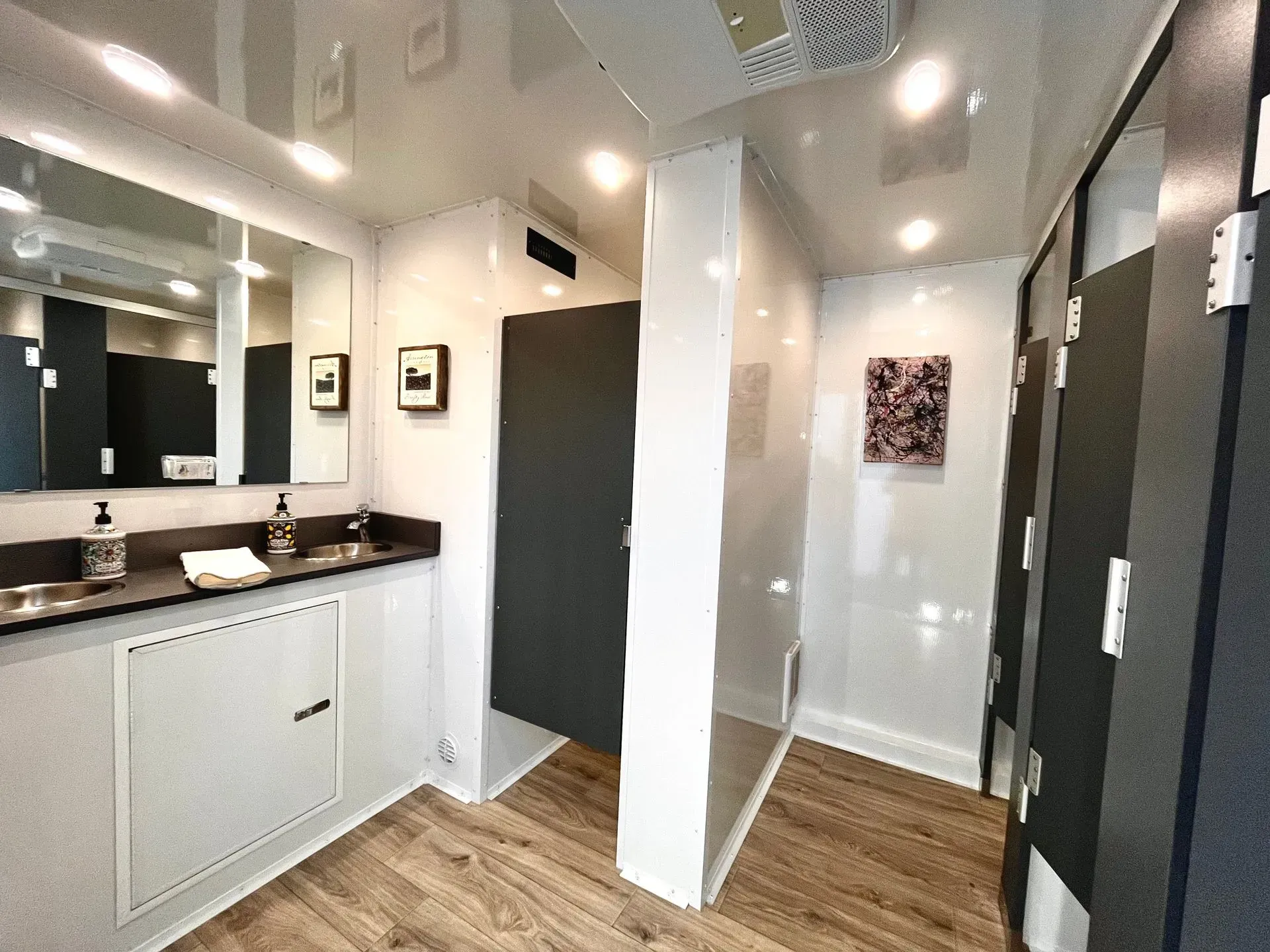 Inside a modern restroom trailer with multiple stalls, sinks, and a mirror.