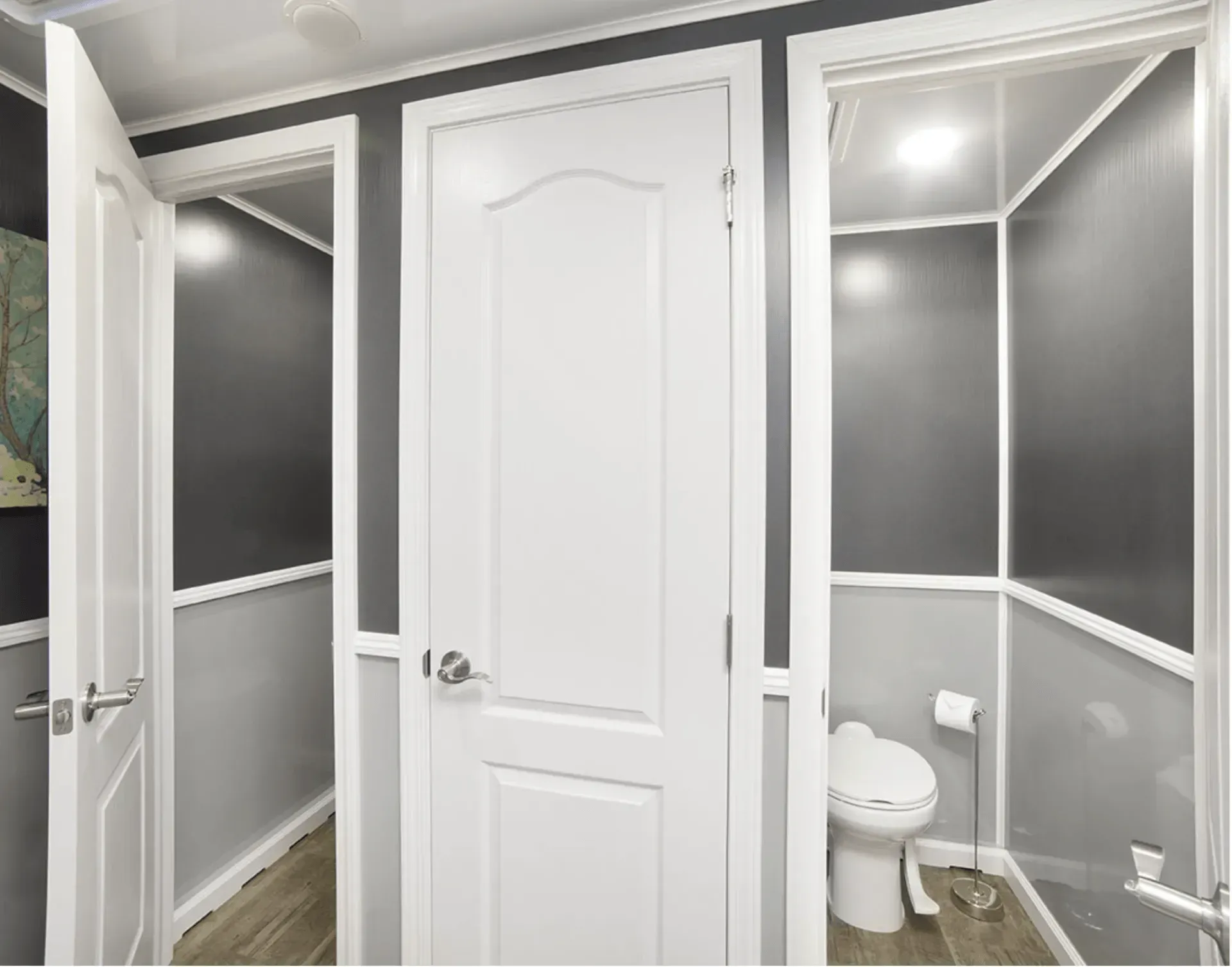 Interior of a trailer with three white-framed doorways. One leads to a hallway, one is closed, and one to a bathroom with a toilet.