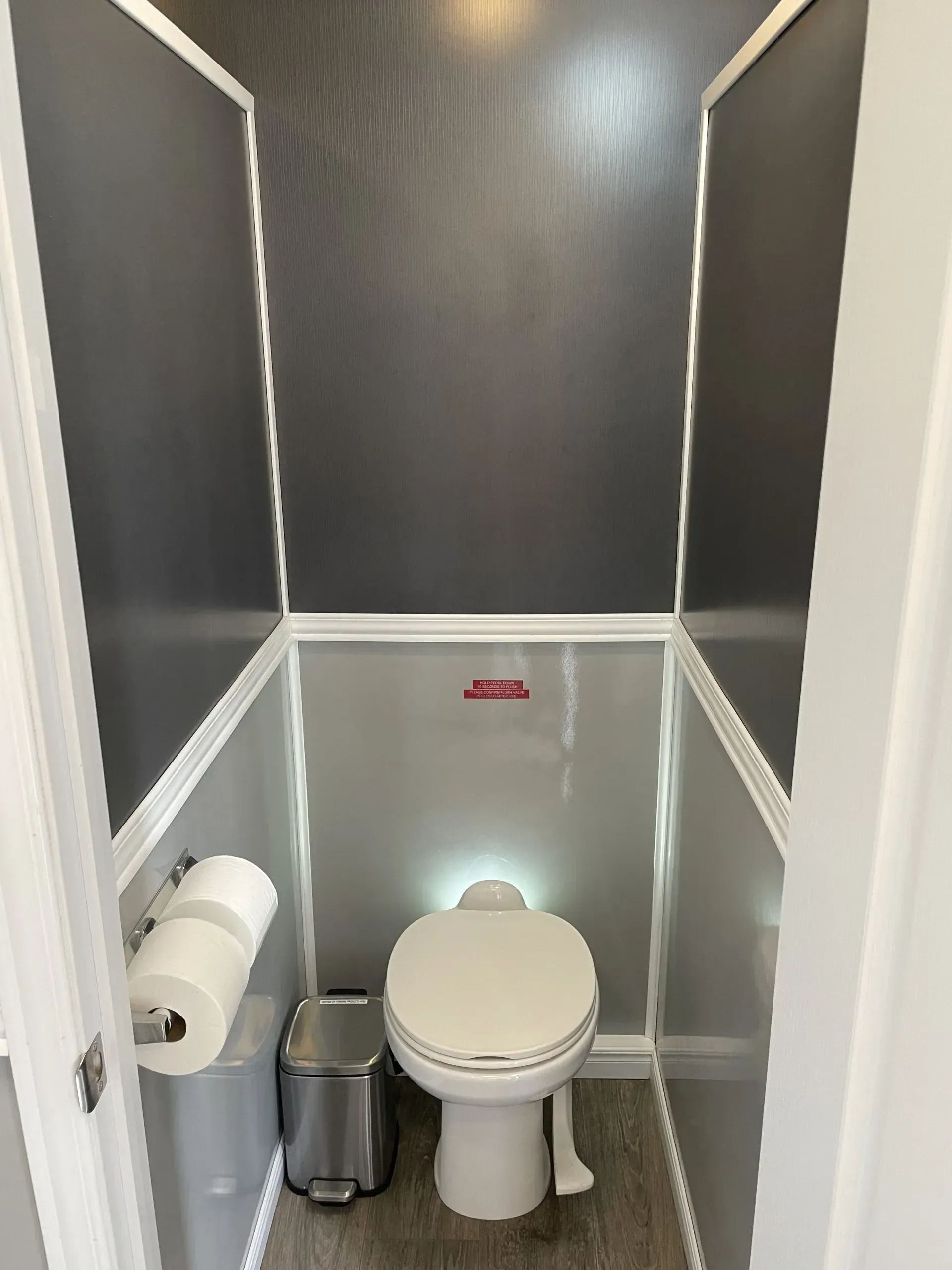 Interior of a portable toilet with gray walls, white trim, a toilet, and a paper towel holder.