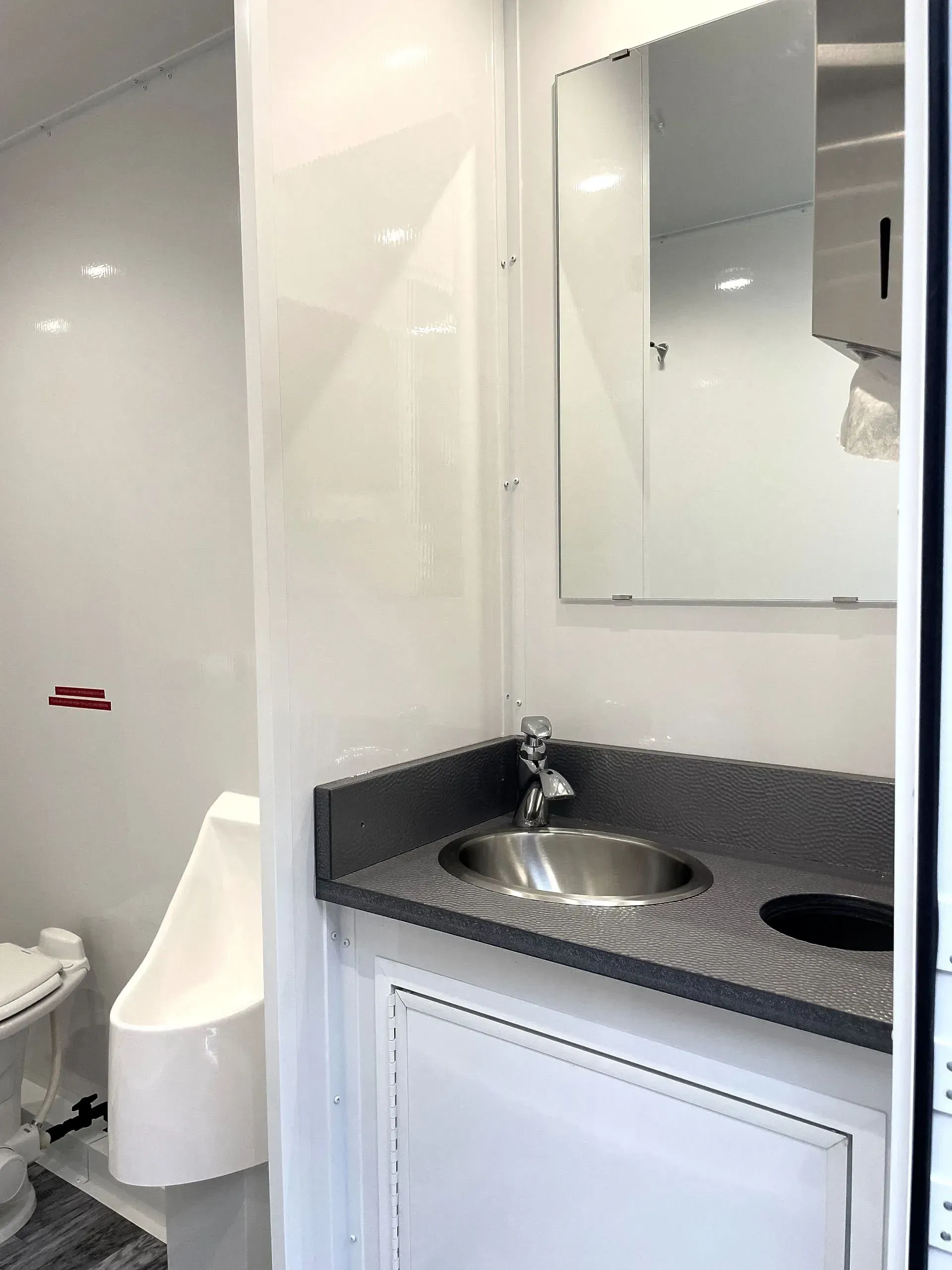 Interior of a clean, white portable restroom with a sink, mirror, and toilet.