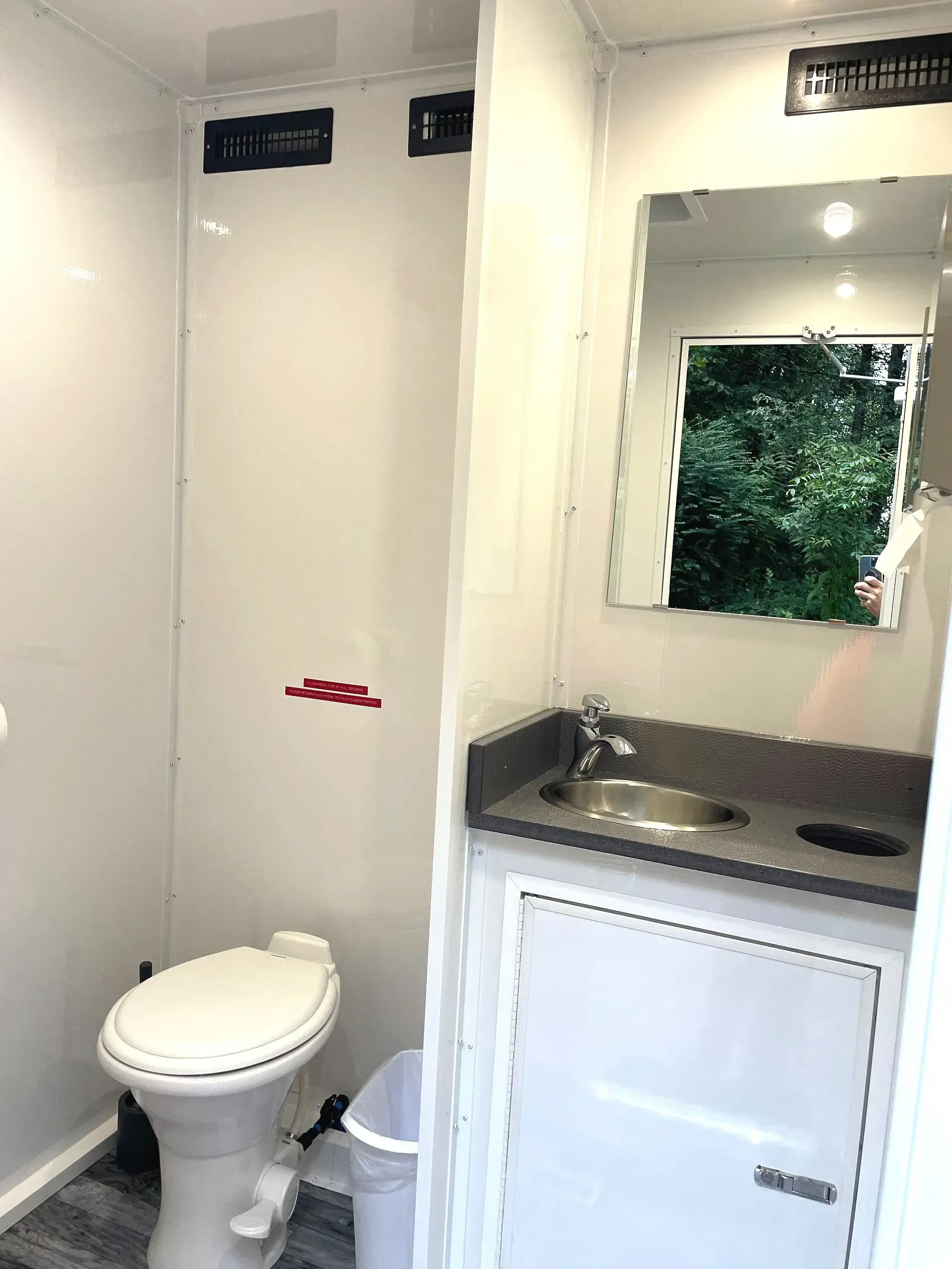 Interior of a portable restroom with a toilet, sink, mirror, and a gray countertop.