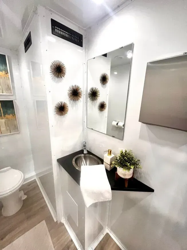 Interior view of a modern portable restroom. Features a sink, mirror, and decorations.