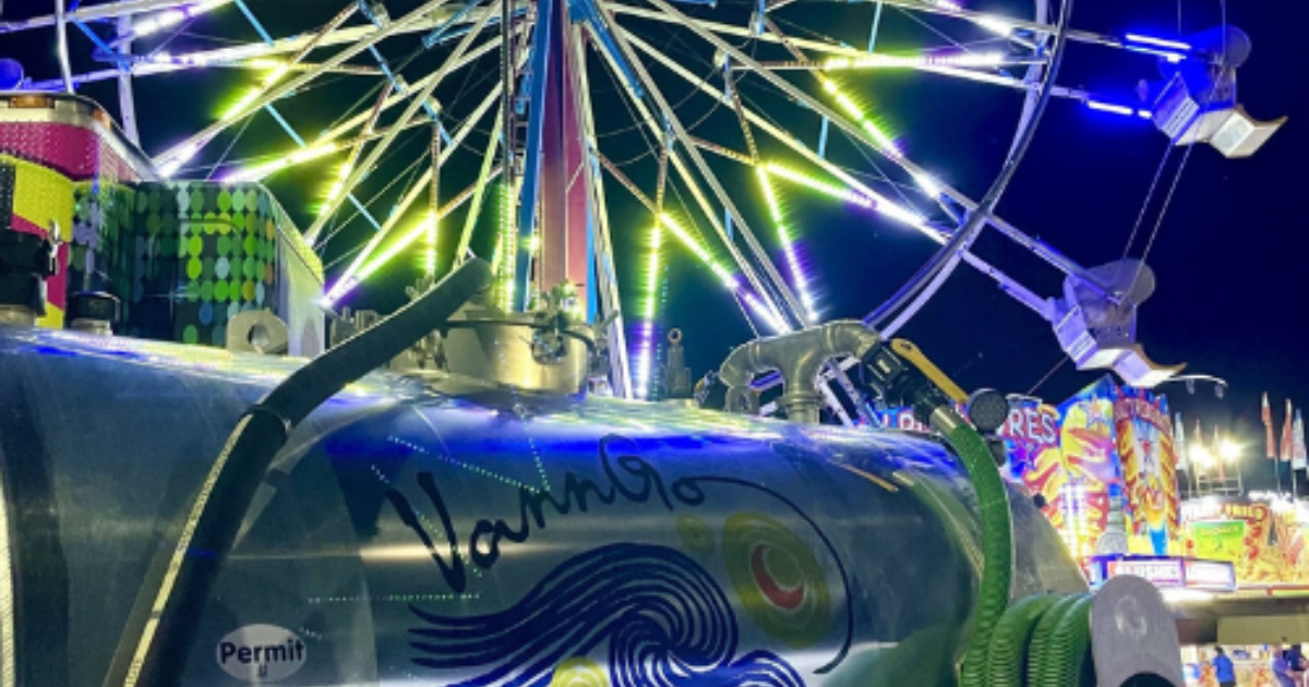 Ferris wheel lit up at night, with a water tank in front displaying the word 