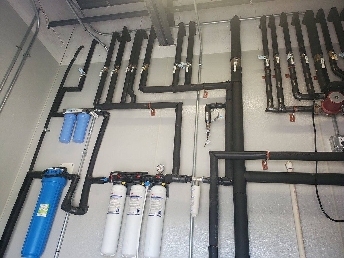 Pipes with black insulation and water filtration system against a white wall.
