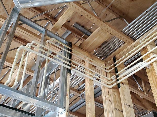 Exposed plumbing and electrical conduits in a building's unfinished ceiling. White pipes and silver conduits are visible.