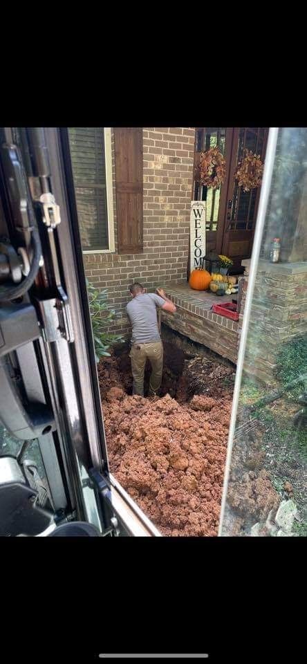 Person digging a hole near a house. Dirt pile is in front. View is from a vehicle.