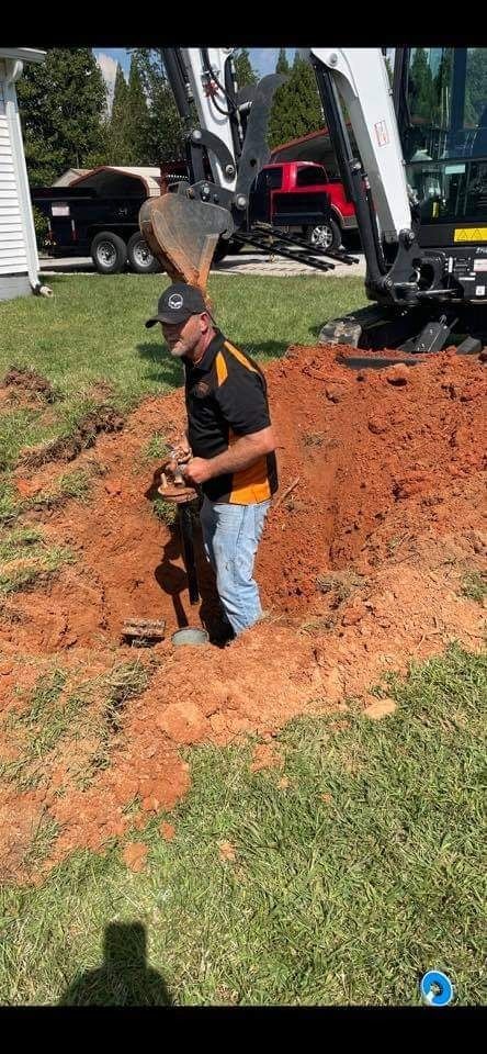 A person standing in a hole, working with excavation equipment in a yard.