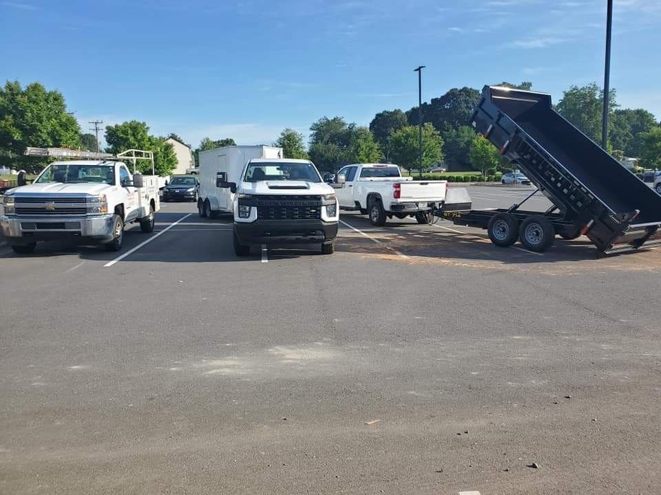 Several pickup trucks parked in a lot; one with a raised dump trailer. Sunny day.