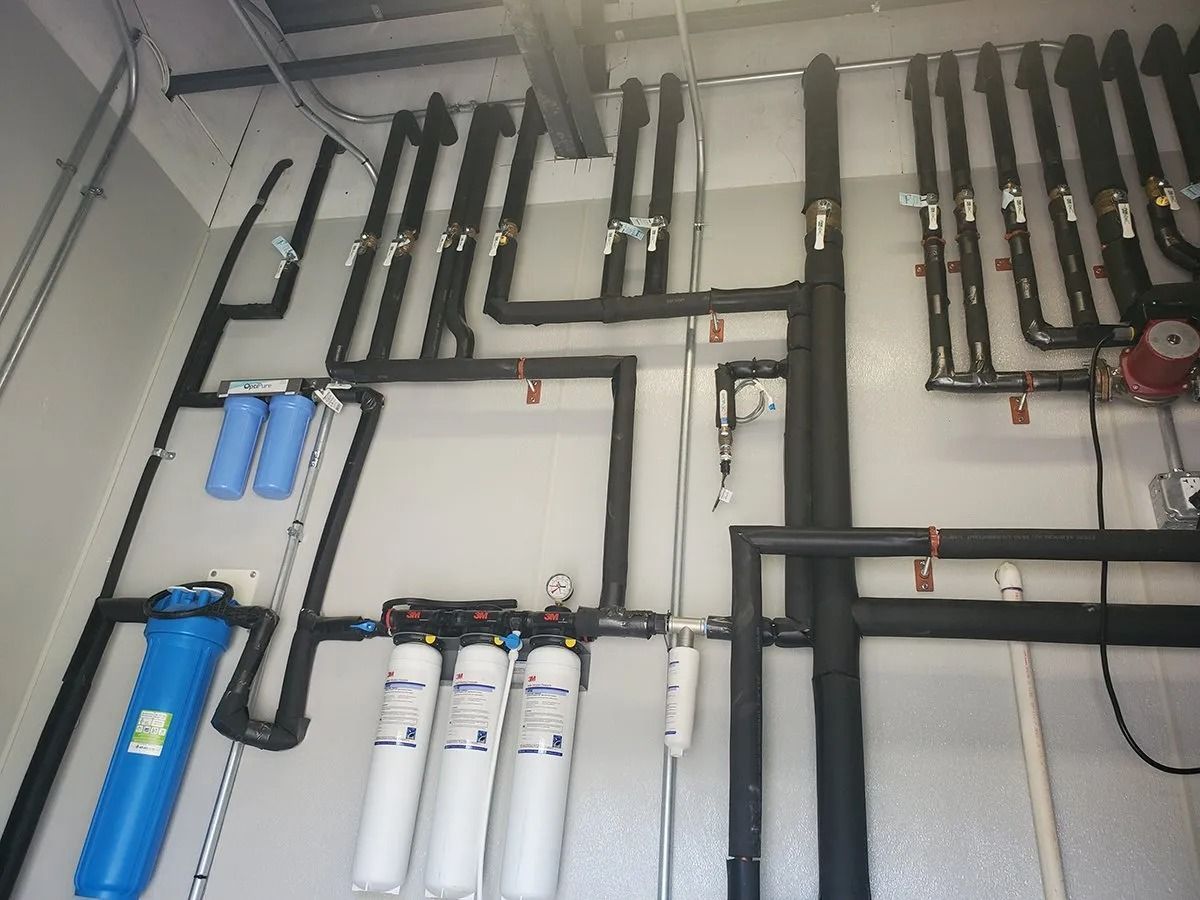 Pipes and water filters mounted on a wall. Black insulated pipes with valves and filter housings in a utility setting.