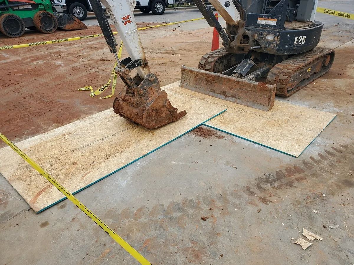 Excavator on wood mats on a concrete surface at a construction site.