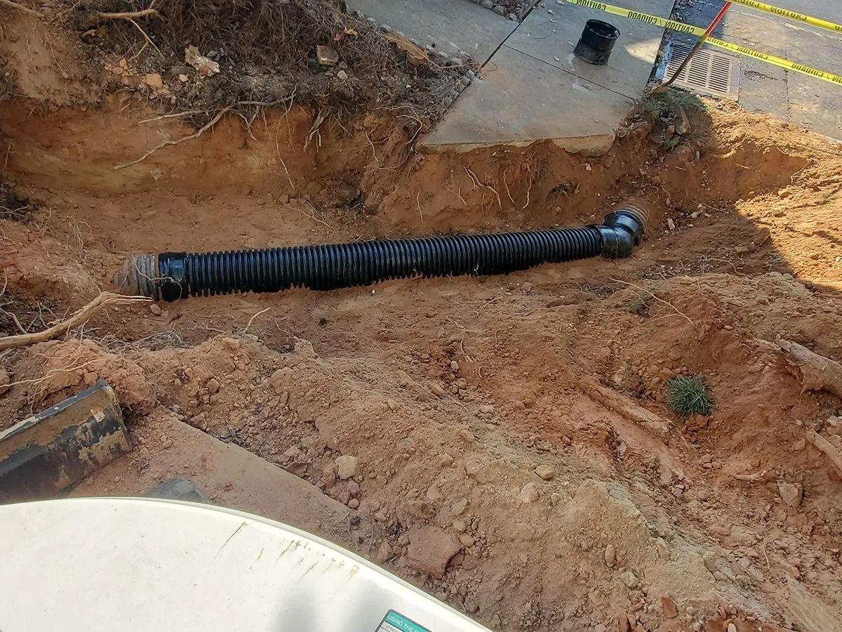 Black corrugated drain pipe in a dirt trench next to concrete.