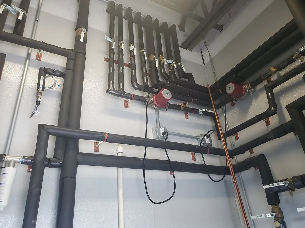 Pipes with black insulation on a white wall; includes pumps, valves, and wiring.