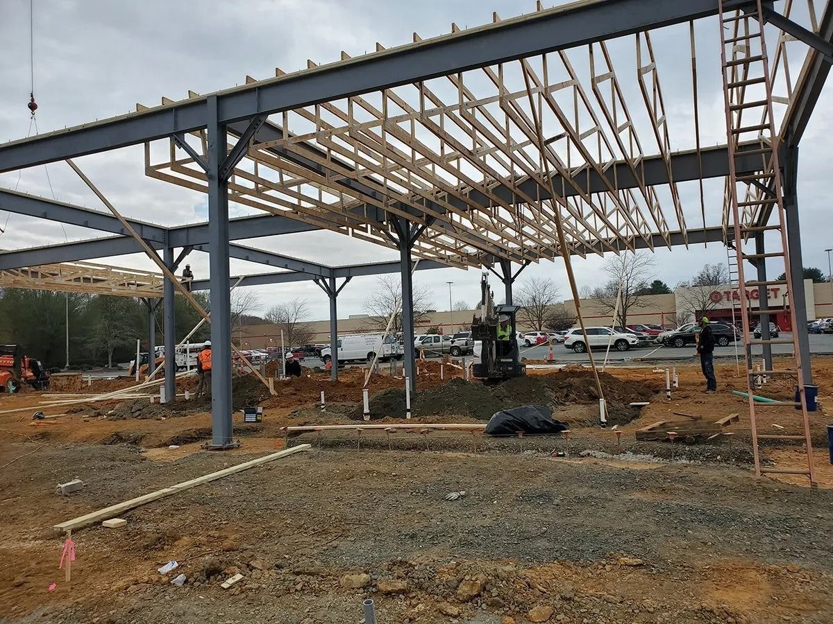Construction site with steel framework, wooden rafters, and earth moving equipment.
