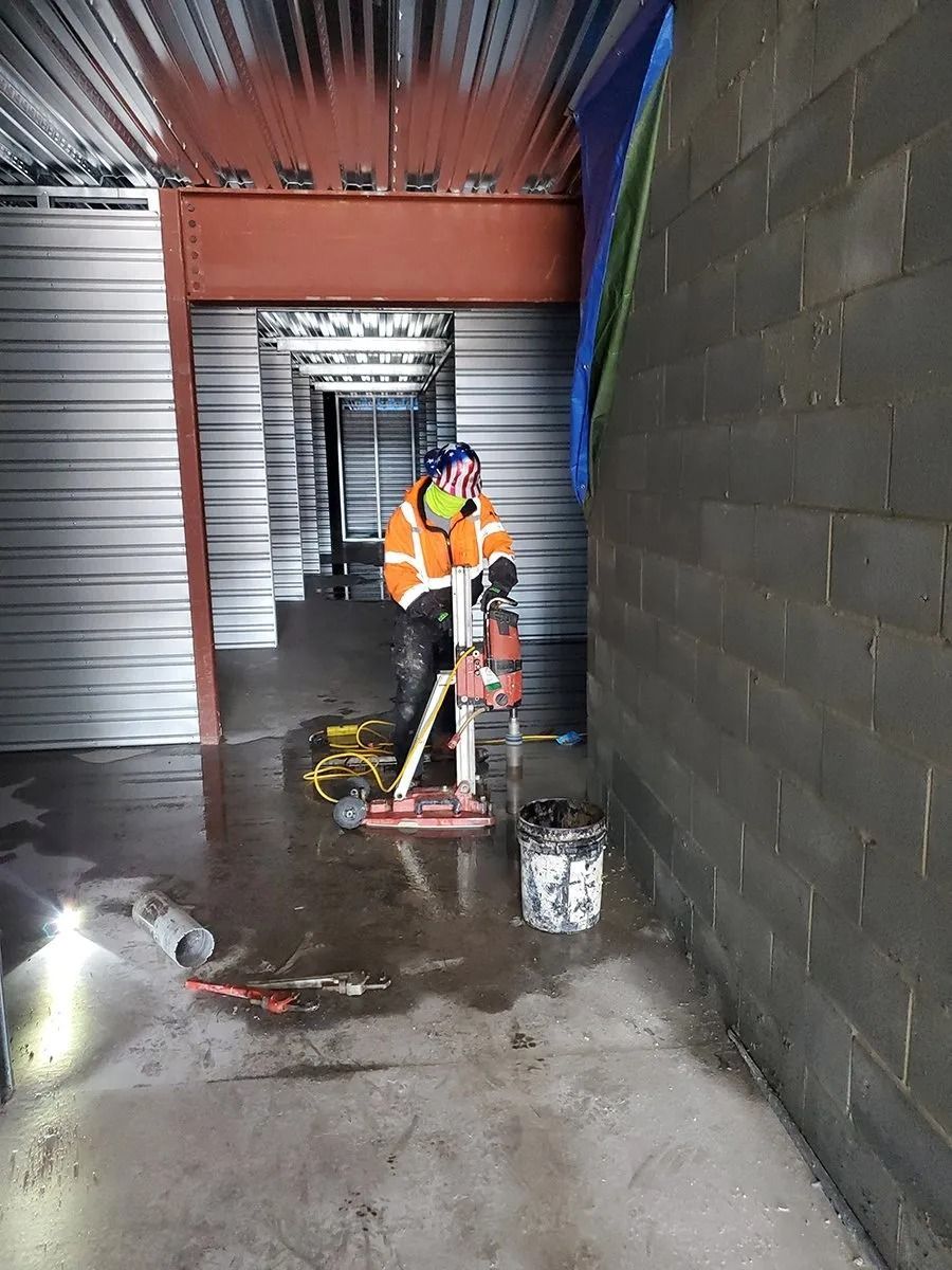 Person drilling a hole in a concrete wall, with tools and water in a construction setting.