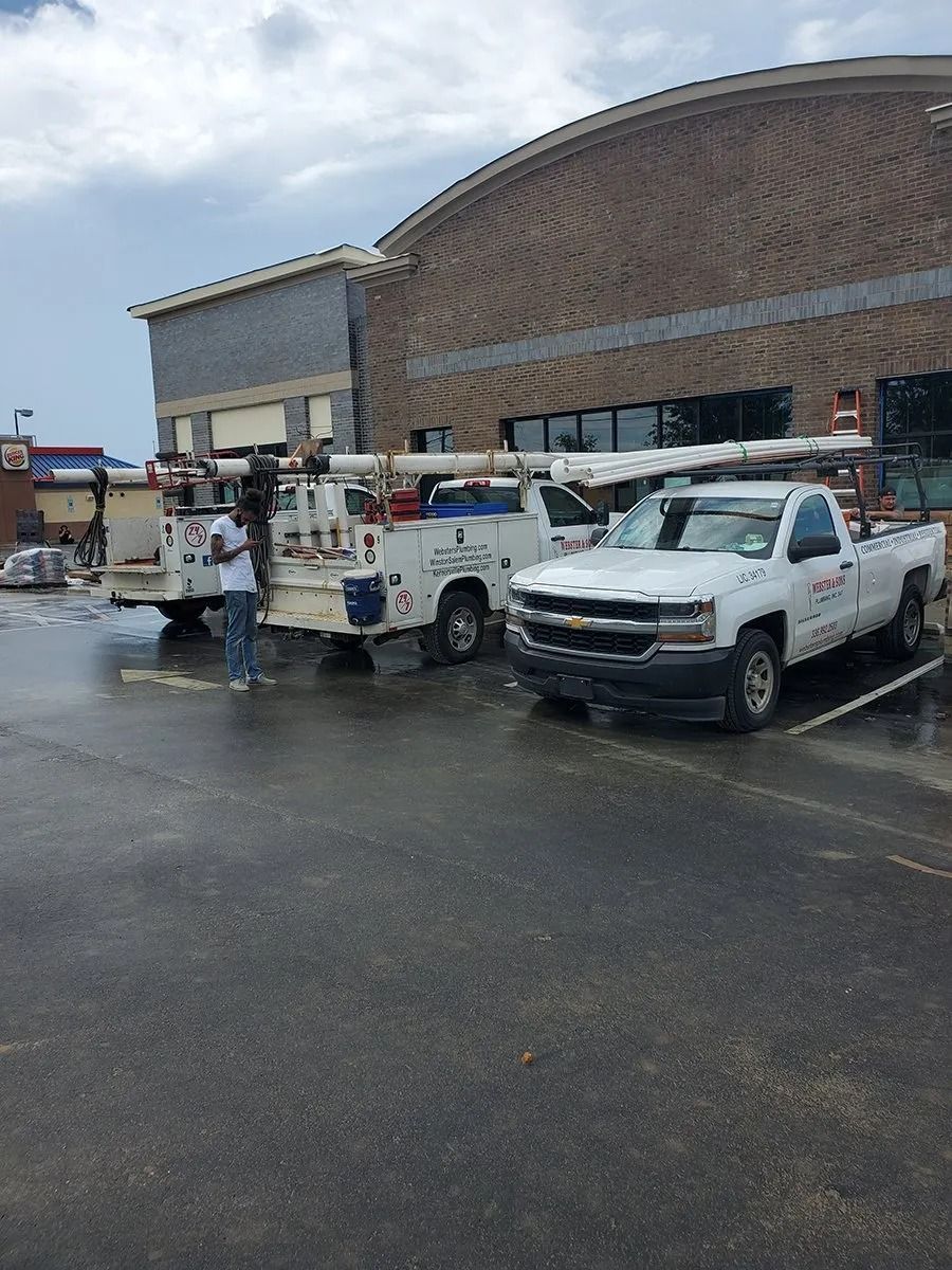 Three white work trucks parked in front of a building; one person stands beside a truck.