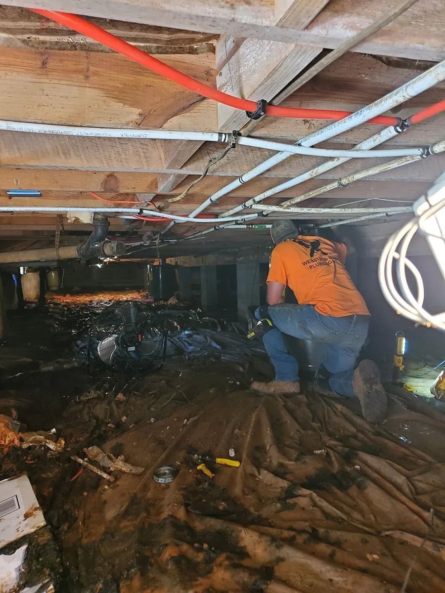 Person inspecting a crawlspace under a home with pipes and debris.