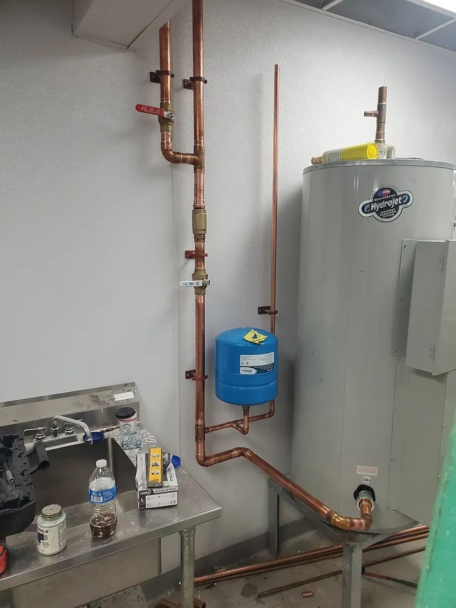 Copper pipes and tank next to a water heater in a utility room.