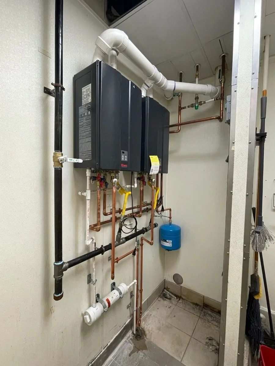 Two black tankless water heaters mounted on a wall with connected pipes and exhaust venting.
