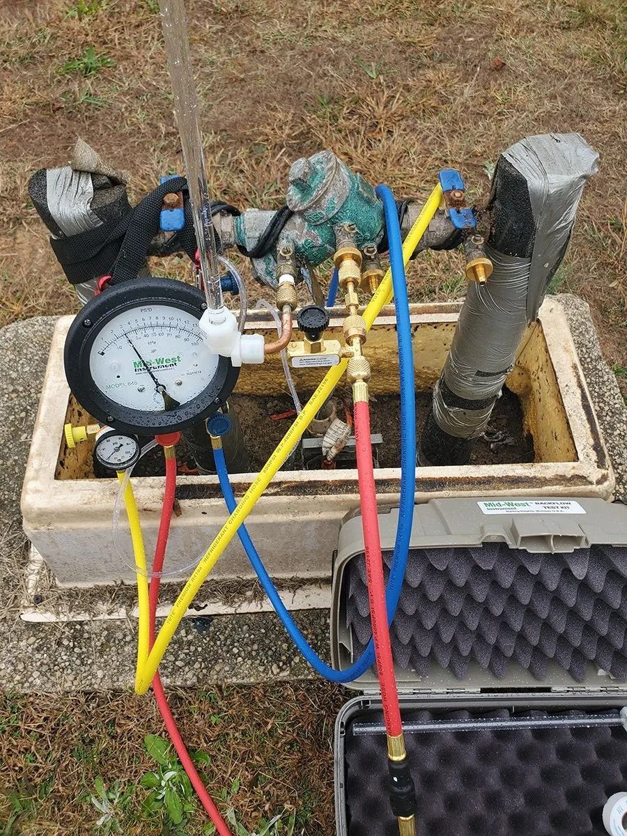 Water meter with gauges and hoses connected, outdoors in a utility box.