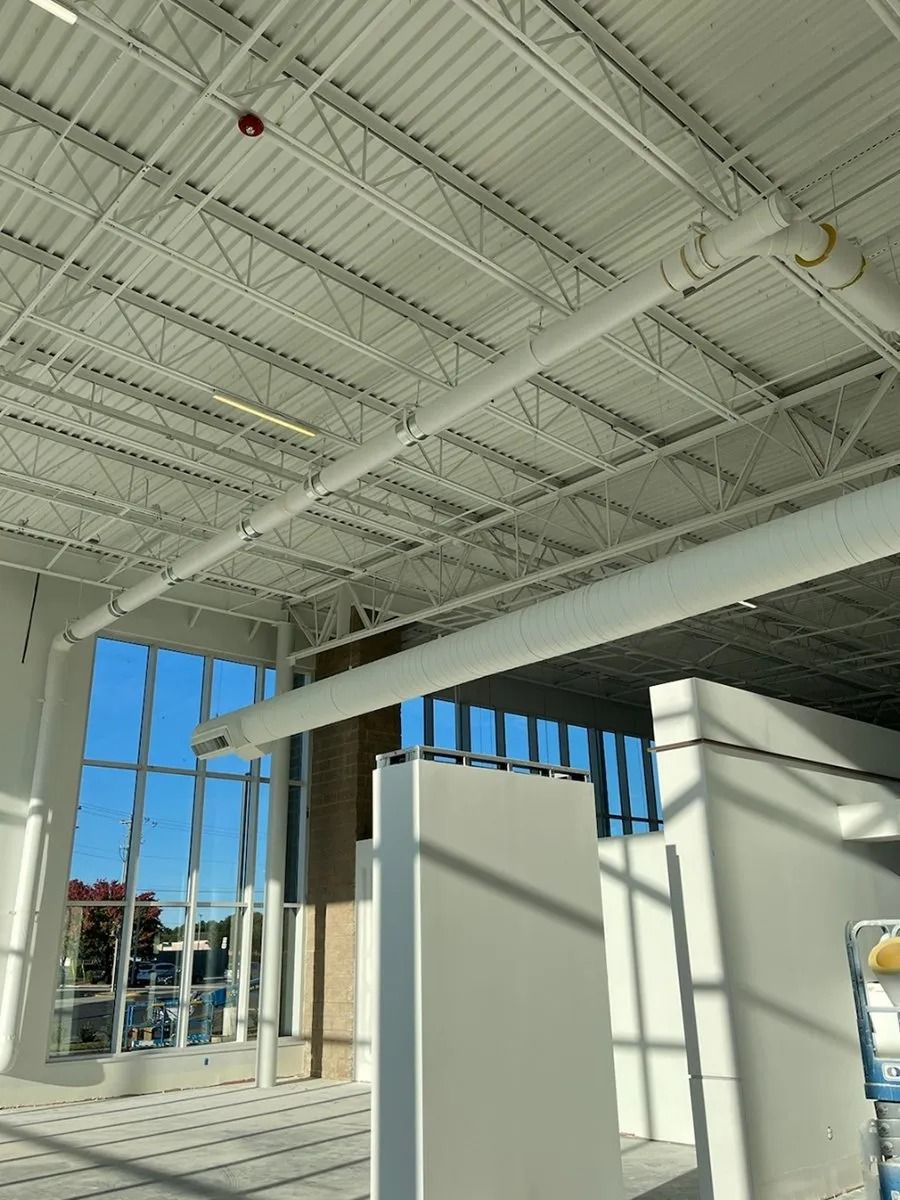 Interior of a white building with large windows, exposed ceiling beams, and rectangular supports.