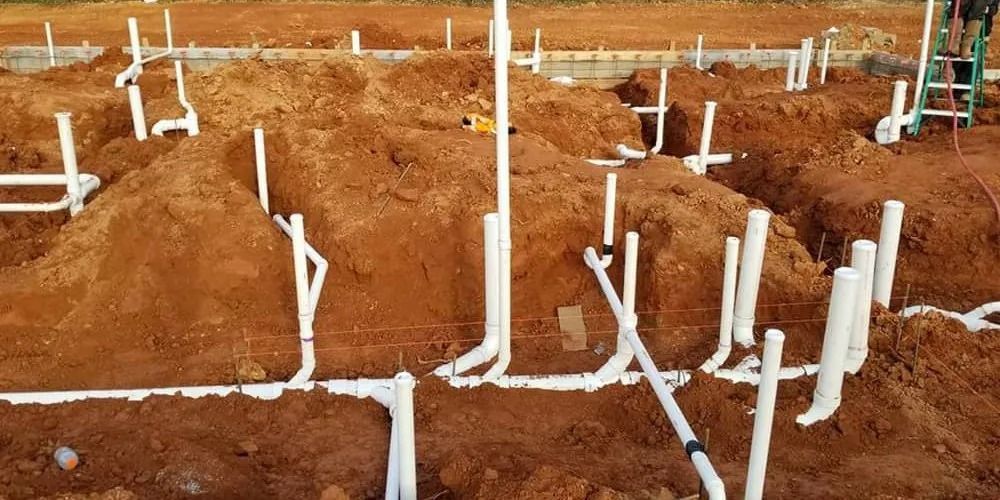 White plumbing pipes emerging from red dirt, likely a construction site.