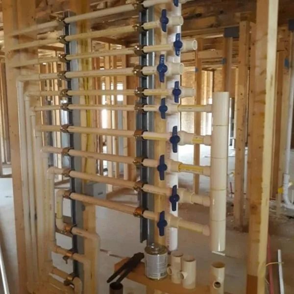 Piping system installed in a framed wall. Beige and blue pipes with valves are visible. The setting is under construction.